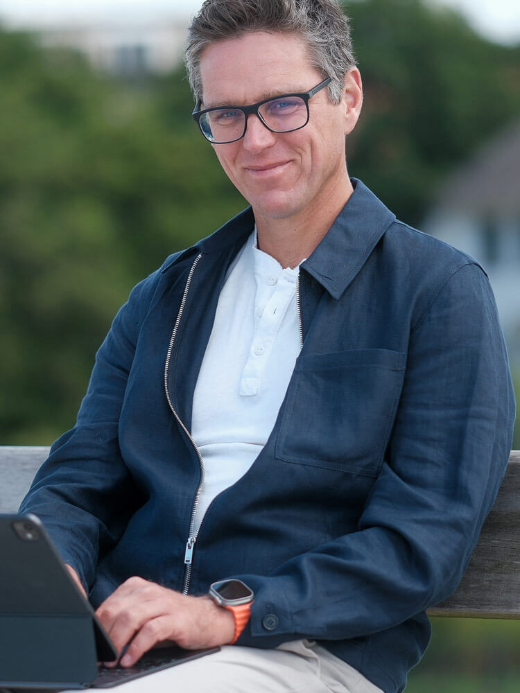 Geschäftsführer Jens Buss sitzt mit einem iPad auf dem Schoß auf einer Bank